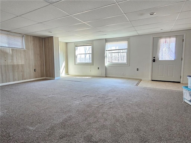 empty room featuring a drop ceiling, baseboards, carpet, and wood walls