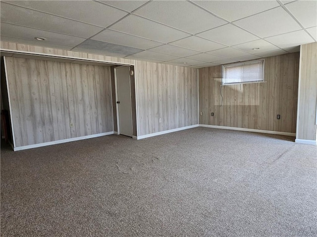 carpeted empty room featuring baseboards, a paneled ceiling, and wood walls