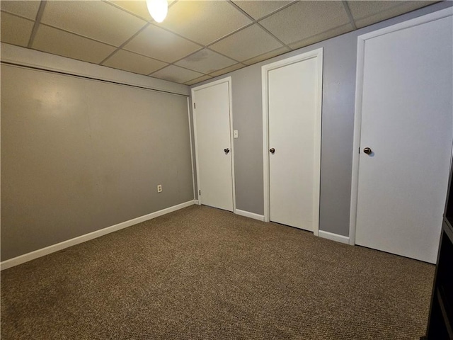 unfurnished bedroom featuring baseboards, a paneled ceiling, and carpet