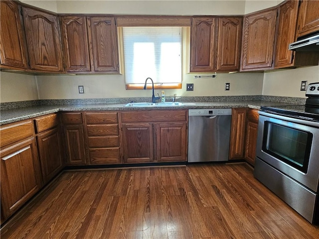 kitchen featuring dark countertops, dark wood-type flooring, under cabinet range hood, appliances with stainless steel finishes, and a sink