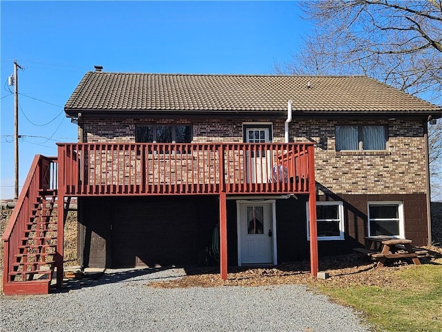 back of property featuring brick siding, a deck, stairs, and a tile roof