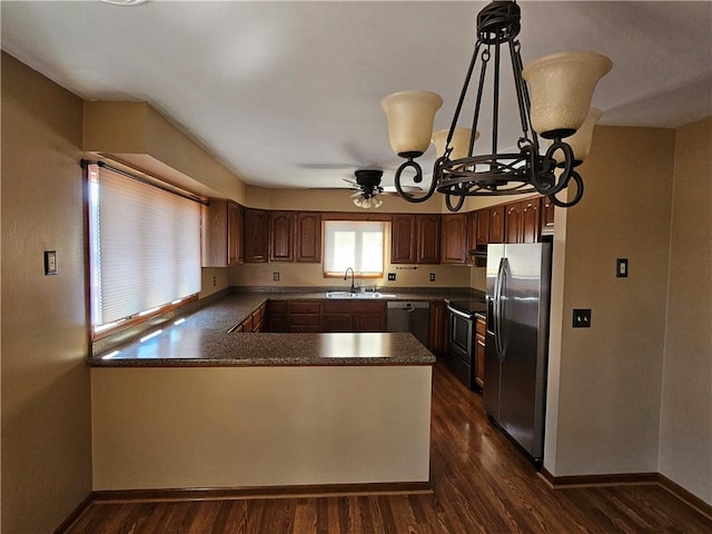 kitchen featuring dark countertops, baseboards, a peninsula, dark wood-style floors, and stainless steel appliances