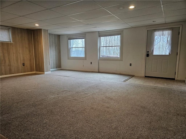 carpeted empty room featuring a drop ceiling, wood walls, and baseboards