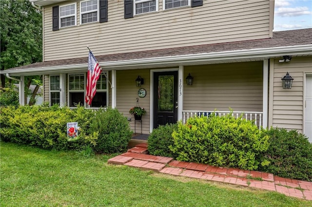 entrance to property featuring covered porch, roof with shingles, and a lawn