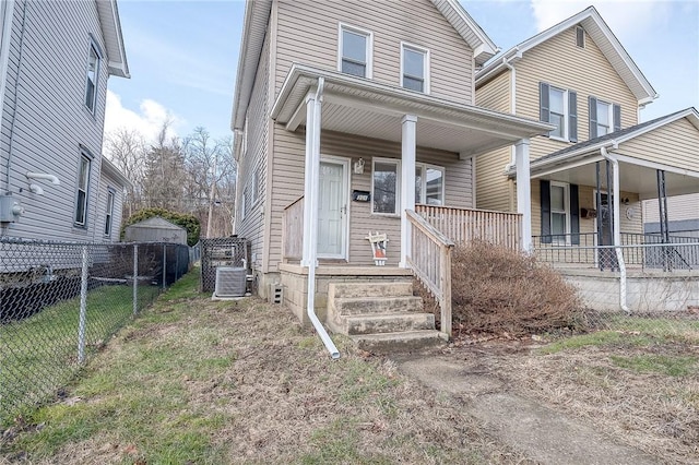 view of front of house with central AC unit, covered porch, fence, and a front yard