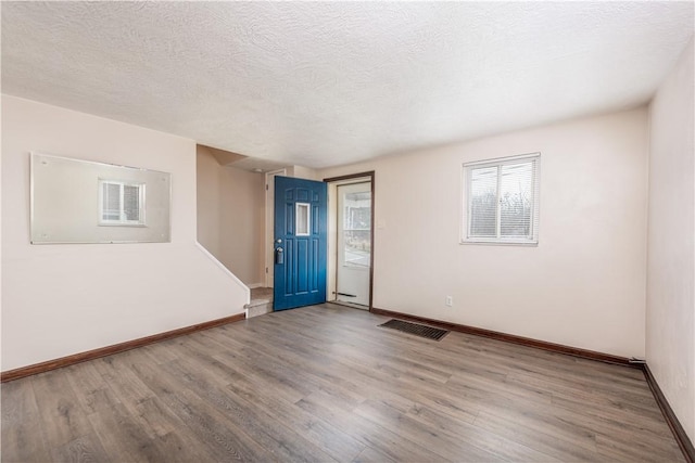 empty room featuring visible vents, a textured ceiling, baseboards, and wood finished floors