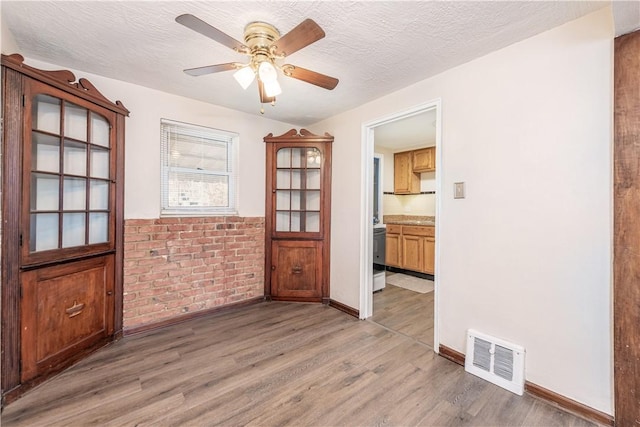 empty room featuring a ceiling fan, visible vents, a textured ceiling, and light wood finished floors