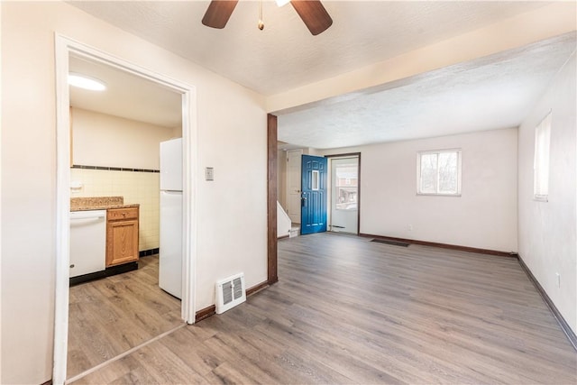 empty room featuring a textured ceiling, visible vents, baseboards, tile walls, and light wood-type flooring