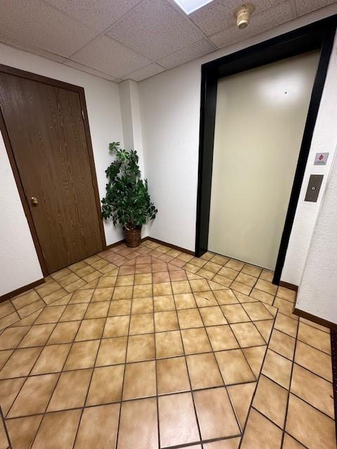 empty room featuring a paneled ceiling, elevator, and baseboards