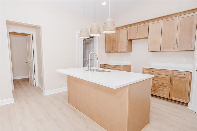 kitchen featuring decorative light fixtures, light wood finished floors, a kitchen island with sink, a sink, and baseboards