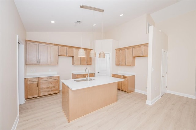 kitchen with hanging light fixtures, light wood finished floors, an island with sink, and a sink