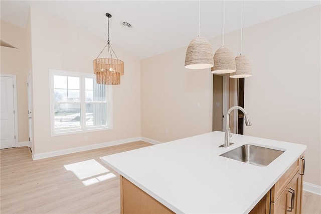 kitchen with pendant lighting, light countertops, a sink, and light wood finished floors