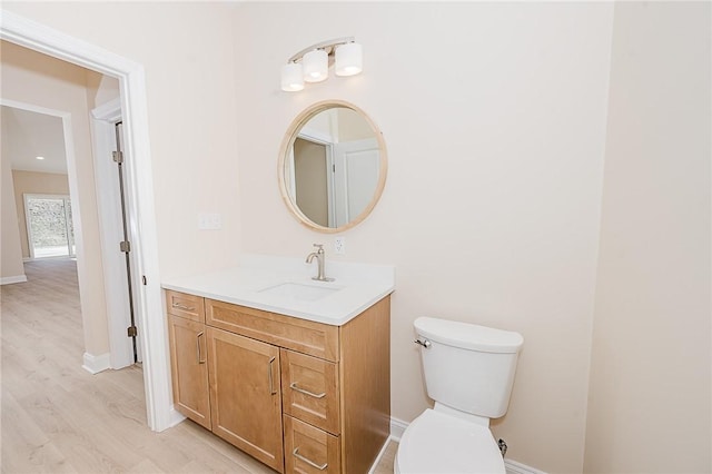 half bathroom with wood finished floors, vanity, toilet, and baseboards