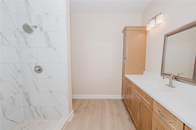 bathroom with baseboards, wood finished floors, tiled shower, and vanity