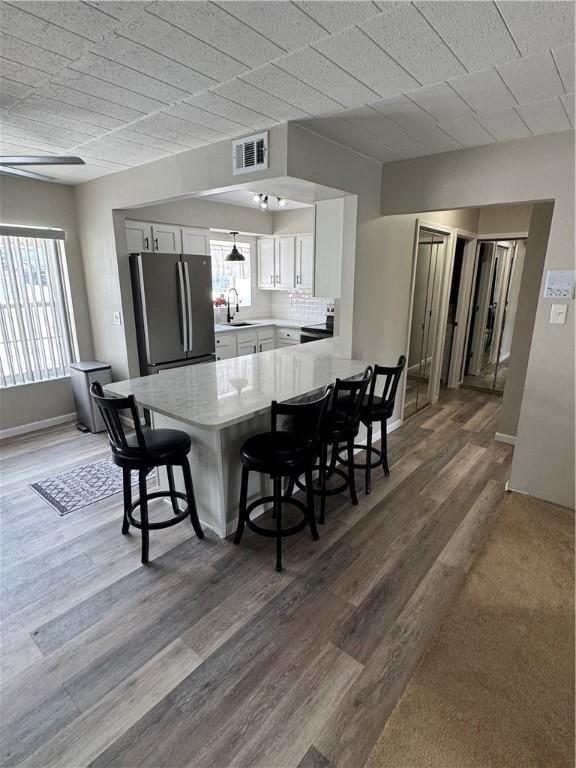 kitchen with visible vents, freestanding refrigerator, a peninsula, light countertops, and a sink