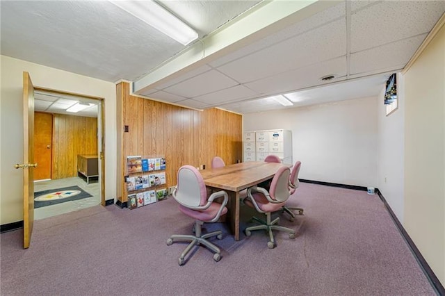 carpeted dining space featuring a paneled ceiling, wood walls, and baseboards