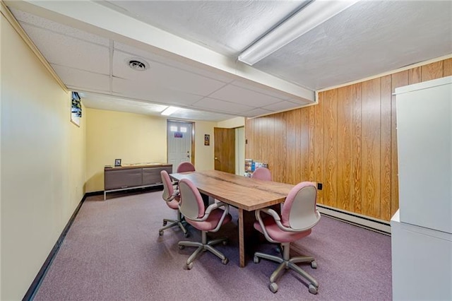 carpeted office with a drop ceiling, a baseboard radiator, visible vents, and wooden walls