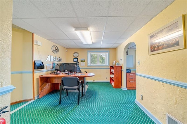office with visible vents, arched walkways, a drop ceiling, a textured wall, and carpet flooring