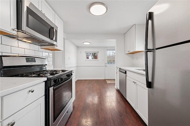 kitchen featuring dark wood finished floors, backsplash, appliances with stainless steel finishes, white cabinets, and baseboards