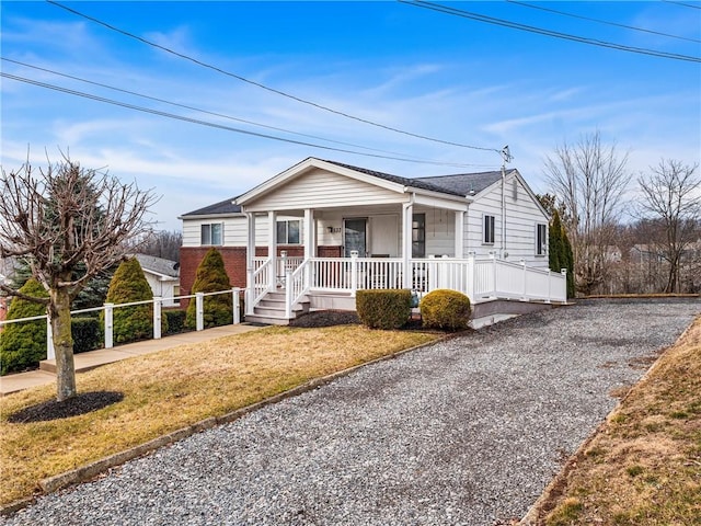 bungalow featuring gravel driveway, covered porch, fence, and brick siding