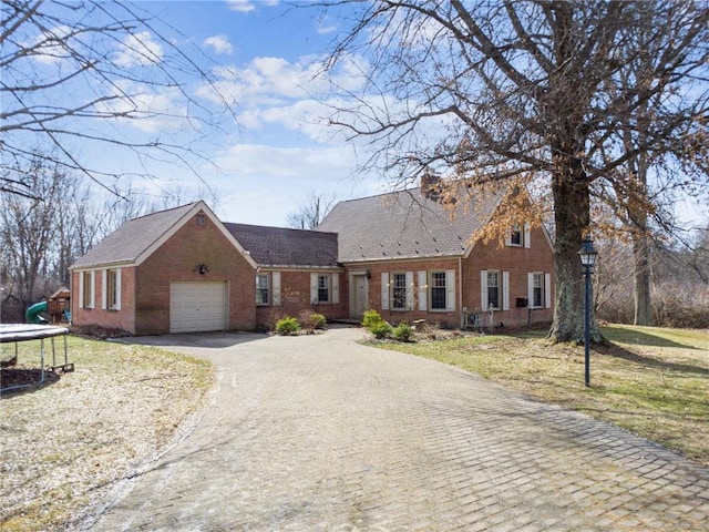 cape cod-style house featuring an attached garage, brick siding, driveway, a front lawn, and a trampoline