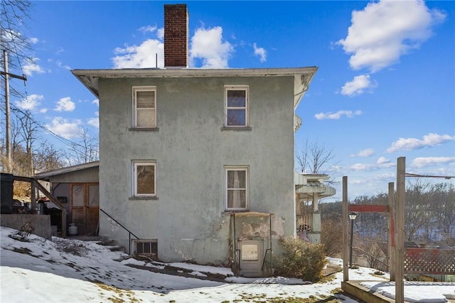 snow covered house featuring a chimney and stucco siding