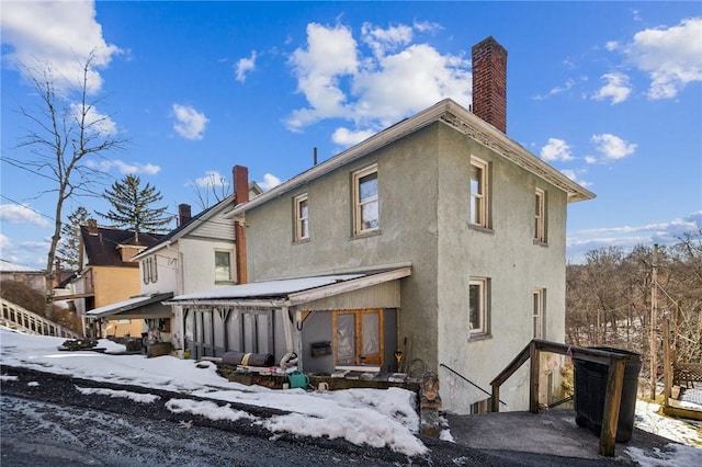 snow covered house featuring a chimney and stucco siding