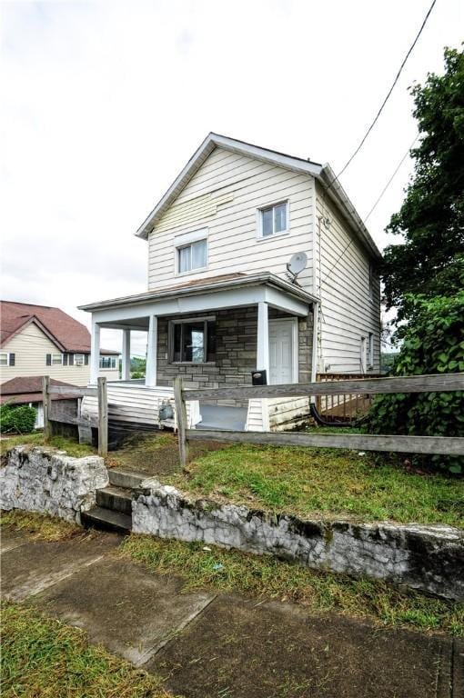 view of front of house with stone siding, fence, and a porch