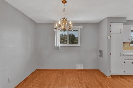 unfurnished dining area with baseboards, an inviting chandelier, visible vents, and light wood-style floors