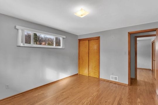 unfurnished bedroom featuring a closet, visible vents, baseboards, and wood finished floors