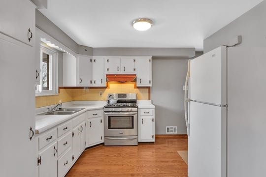 kitchen with under cabinet range hood, a sink, visible vents, freestanding refrigerator, and gas stove