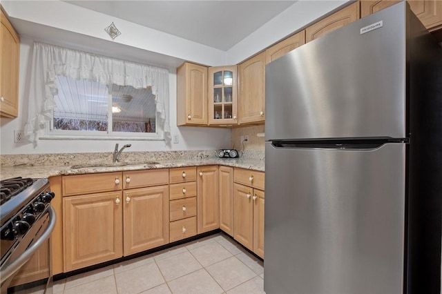 kitchen featuring light tile patterned floors, stainless steel appliances, a sink, light stone countertops, and glass insert cabinets