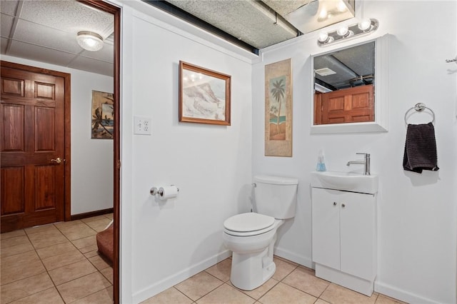 bathroom featuring a paneled ceiling, toilet, vanity, baseboards, and tile patterned floors