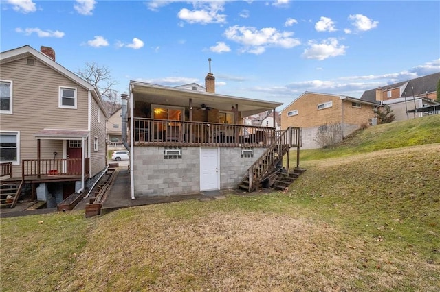 rear view of house with a ceiling fan, a lawn, and stairs