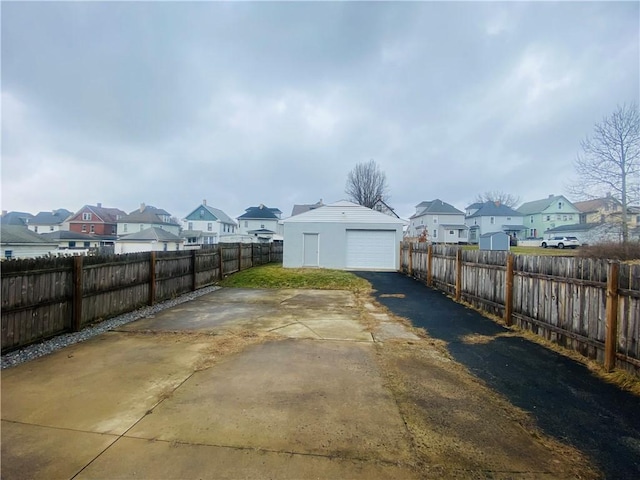 view of yard featuring driveway, a garage, a fenced backyard, a residential view, and an outbuilding