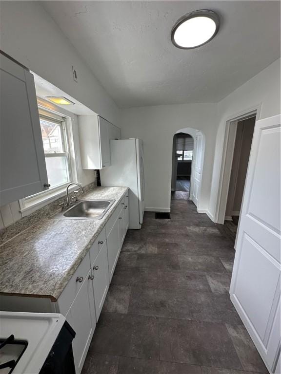 kitchen featuring arched walkways, freestanding refrigerator, white cabinetry, a sink, and baseboards