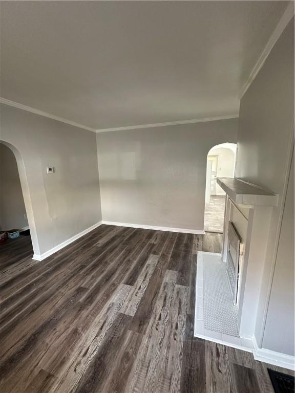 unfurnished living room featuring ornamental molding, arched walkways, dark wood finished floors, and baseboards