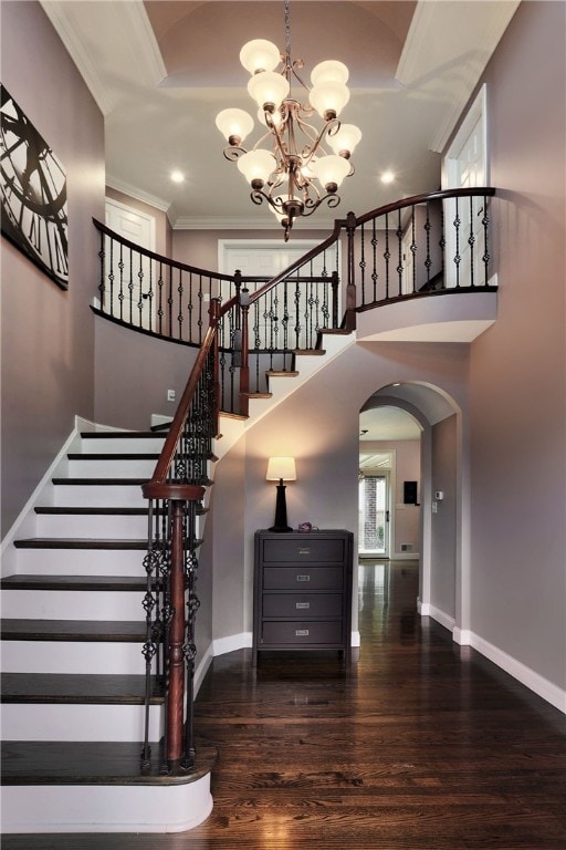 staircase with baseboards, arched walkways, crown molding, and wood finished floors