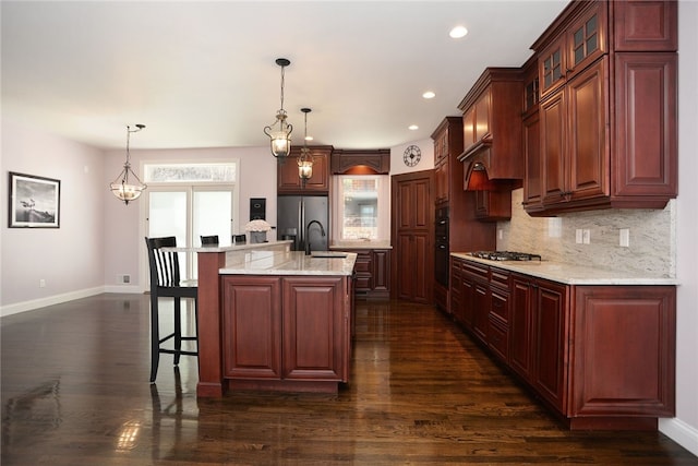 kitchen with dark wood-style floors, a breakfast bar area, backsplash, appliances with stainless steel finishes, and a sink