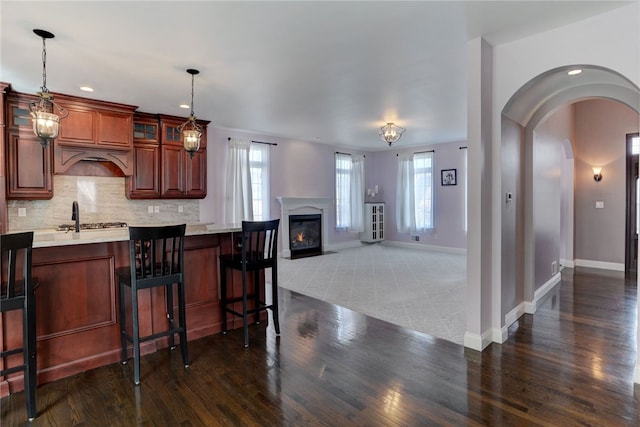 kitchen with tasteful backsplash, arched walkways, pendant lighting, and glass insert cabinets