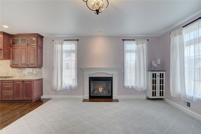 unfurnished living room with dark colored carpet, a fireplace with flush hearth, visible vents, and baseboards