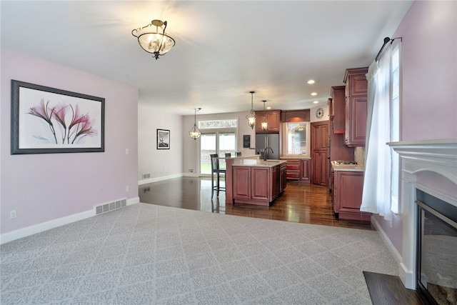 kitchen with stainless steel fridge, baseboards, visible vents, a fireplace with flush hearth, and light countertops