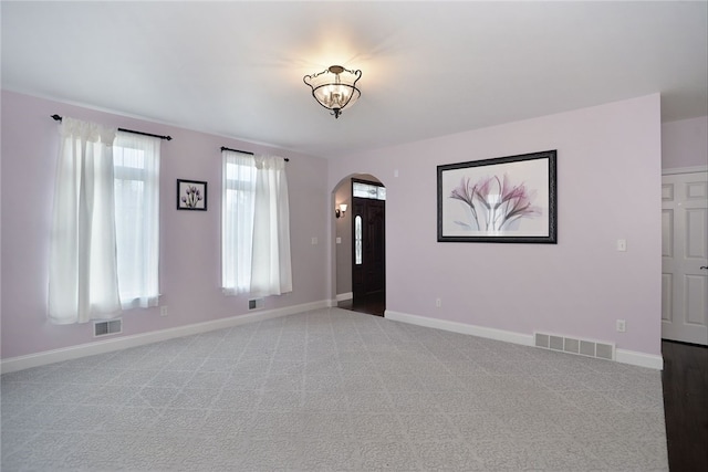 carpeted empty room featuring arched walkways, visible vents, and baseboards