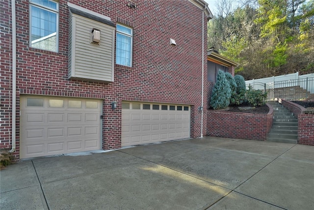 view of property exterior featuring driveway, a garage, fence, and brick siding