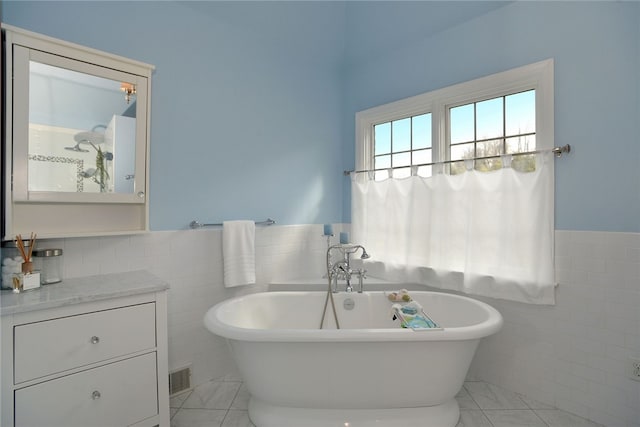 bathroom featuring a wainscoted wall, visible vents, tile walls, and a freestanding bath