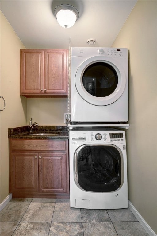 laundry room with stacked washer and clothes dryer, cabinet space, a sink, and baseboards