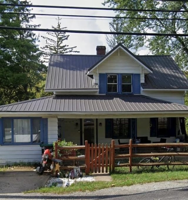 view of front of property with metal roof, a porch, a chimney, and a fenced front yard