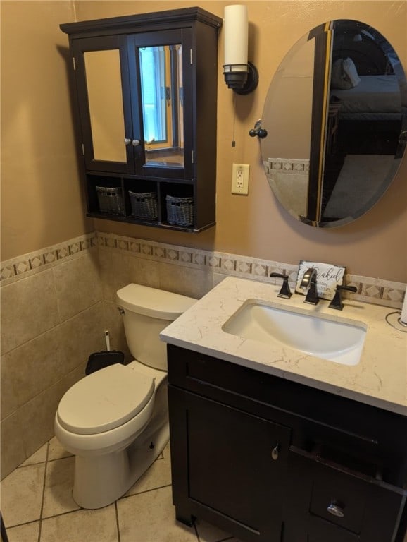 half bath with tile walls, tile patterned flooring, a wainscoted wall, vanity, and toilet