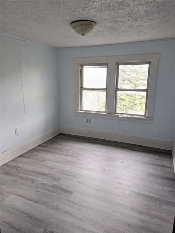spare room with a textured ceiling, wood finished floors, and baseboards
