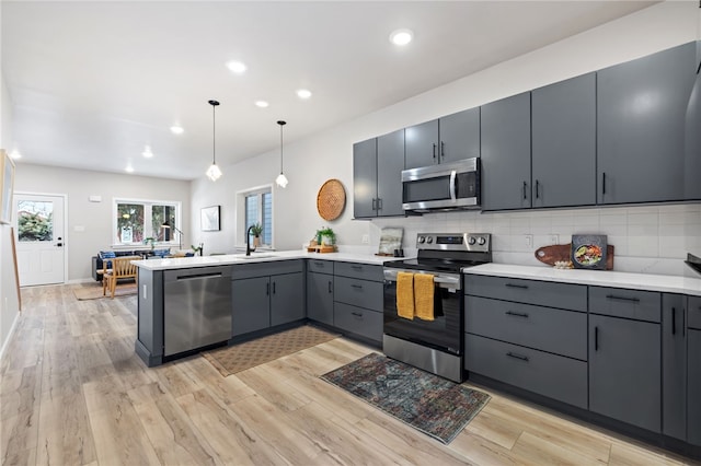 kitchen featuring a peninsula, appliances with stainless steel finishes, light wood-type flooring, and a sink